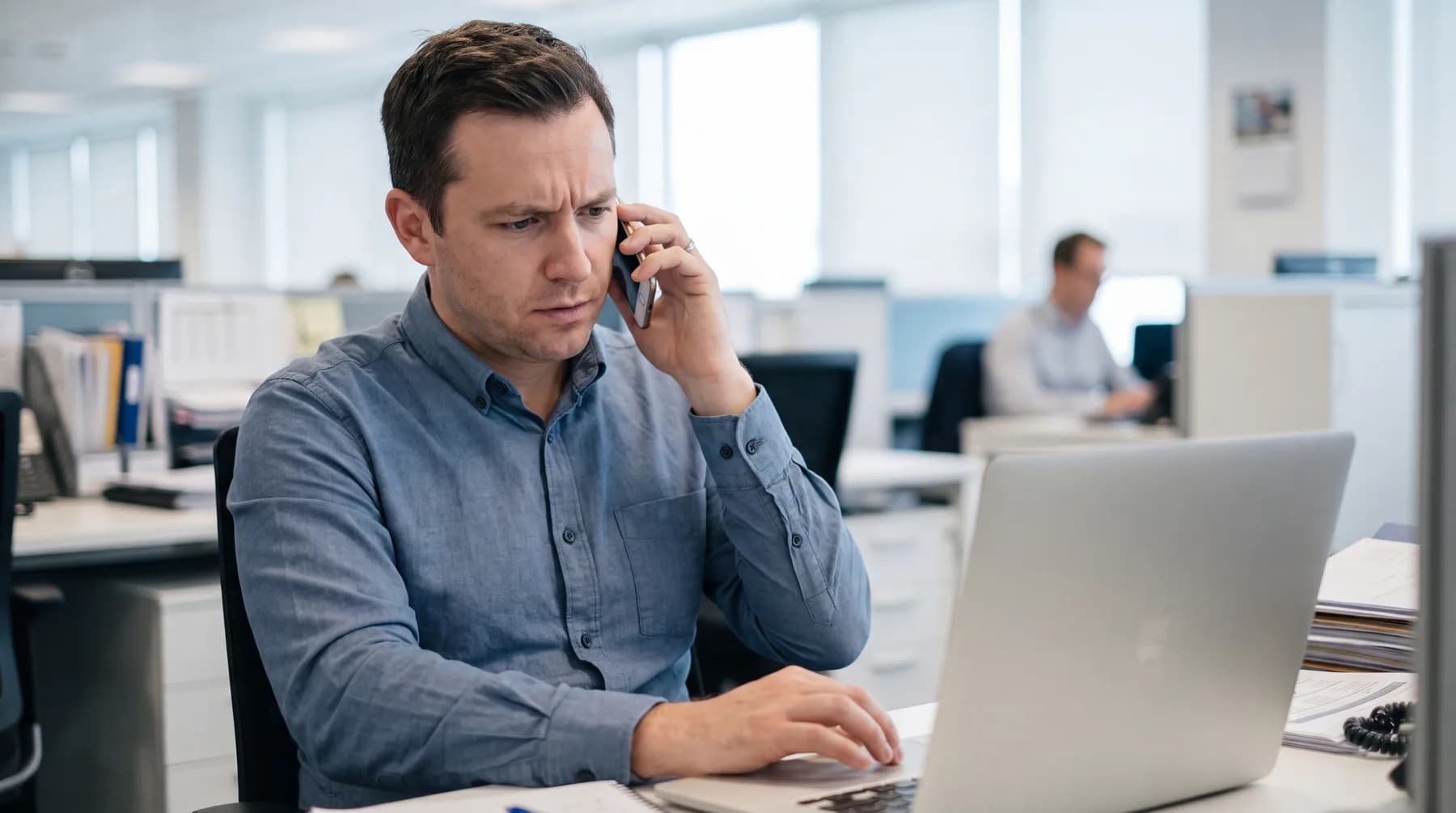Mitarbeiter beschreibt am Telefon ein Problem, während er am Laptop arbeitet.